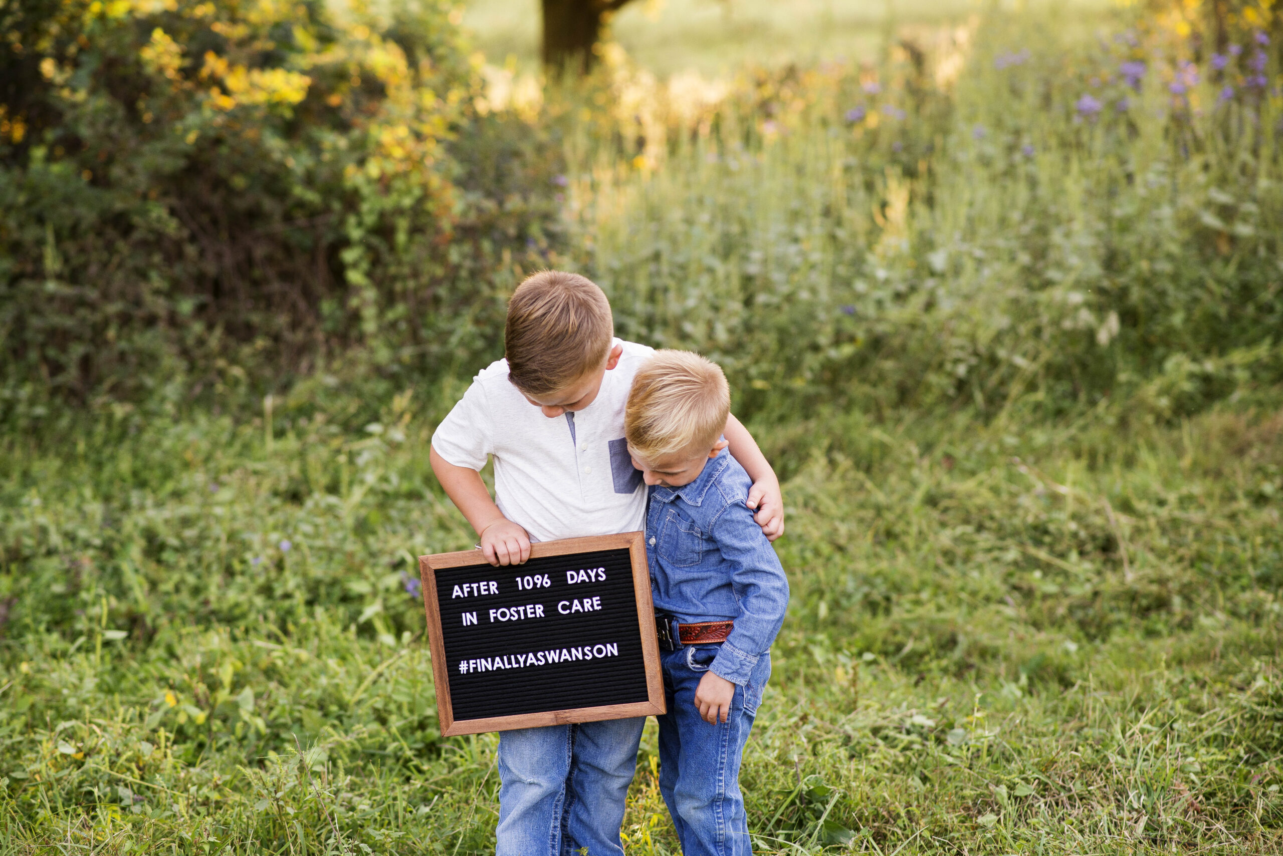 portrait of two brothers hugging, holding an adopted celebration sign