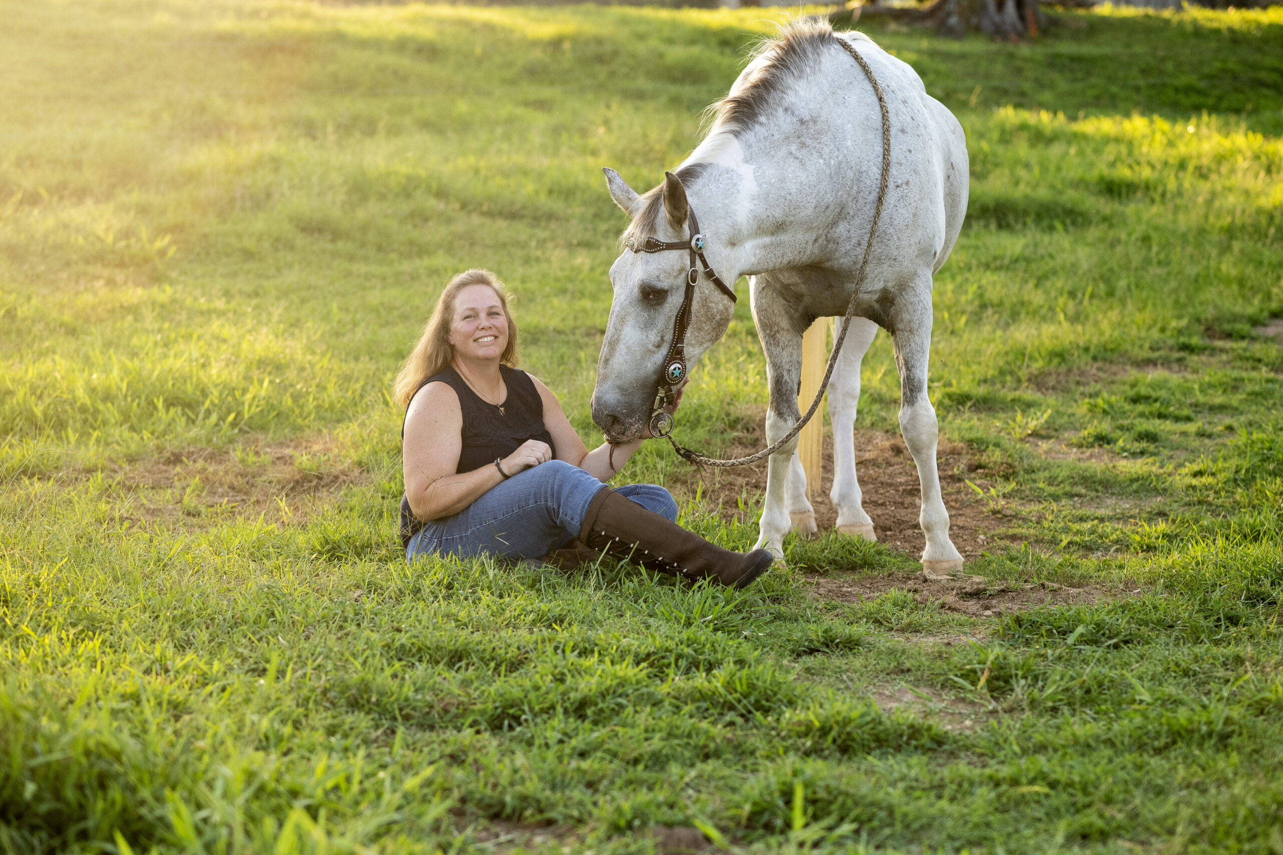 smiling woman sitting in field with horse looking at her